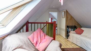 A cozy attic bedroom with a sloped ceiling, a wooden staircase, and a bookshelf.