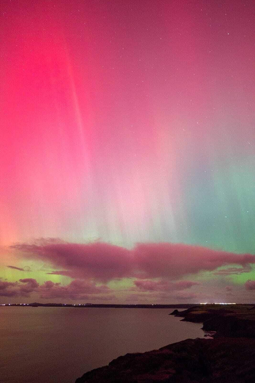 Cielo nocturno con una aurora boreal vibrante sobre un paisaje costero.