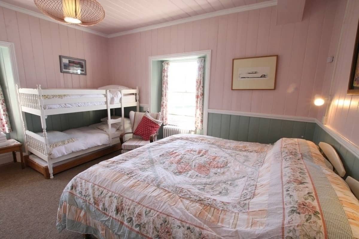 A bedroom with bunk beds, a large bed, a chair, and a window with curtains.