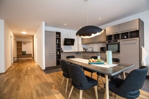 A modern kitchen with a dining area, featuring a wooden floor, dark chairs, and a central island with a fruit bowl. - Ferienwohnung Pfänder (Friedrichshafen)