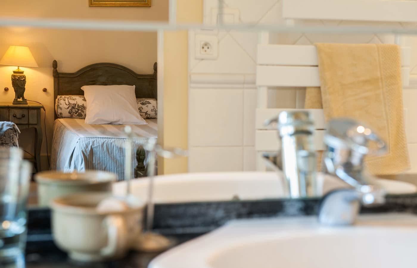 Un dormitorio con cama, mesita de noche, lámpara y baño con lavamanos y espejo.