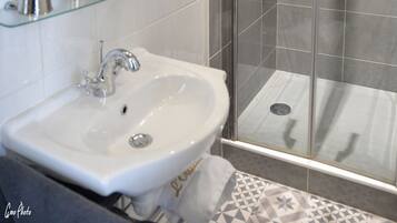 A bathroom with a glass shower enclosure, a sink, and a mirror.
