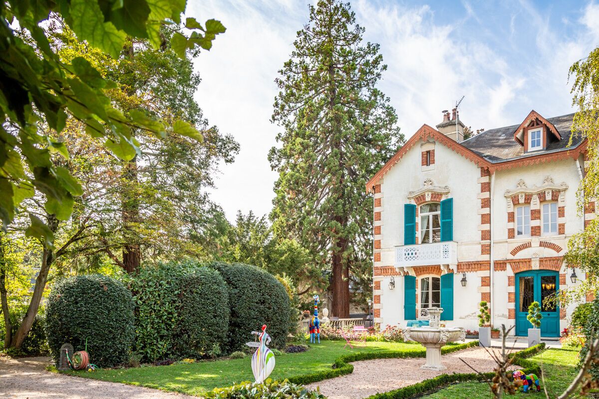 A large, white building with red brick accents and blue shutters, surrounded by lush greenery and a well-maintained garden.