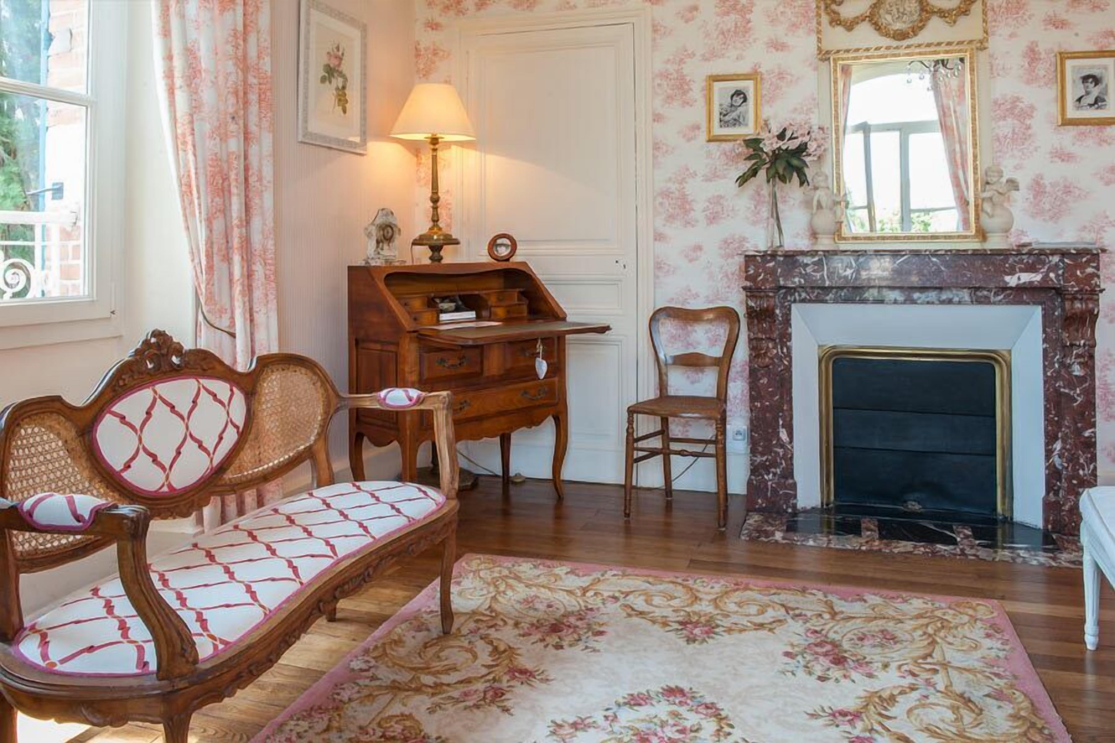 A room with a wooden sofa, a small wooden table, a chair, a fireplace, and a floral rug.