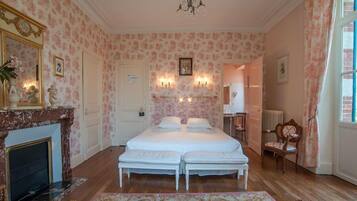 A bedroom with a double bed, a fireplace, a chandelier, and floral wallpaper.