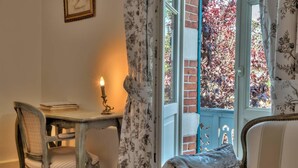 A room with a wooden desk, a chair, a lit candle, and a window with a view of red foliage. - L'Oustal (Bourges)