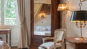 A bedroom with a large mirror, a bedside lamp, a chair, and a window with curtains. - L'Oustal (Bourges)