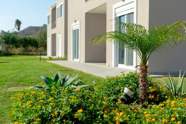 A modern building with a well-maintained lawn and a palm tree in the foreground. - L&C Apartments (Rhodes)
