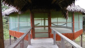 Una estructura de madera con techo de paja, una escalera de madera que conduce a una puerta, y vistas de la vegetación circundante.