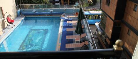 Una piscina en la azotea con sillones de descanso y sombrillas, rodeada de edificios.