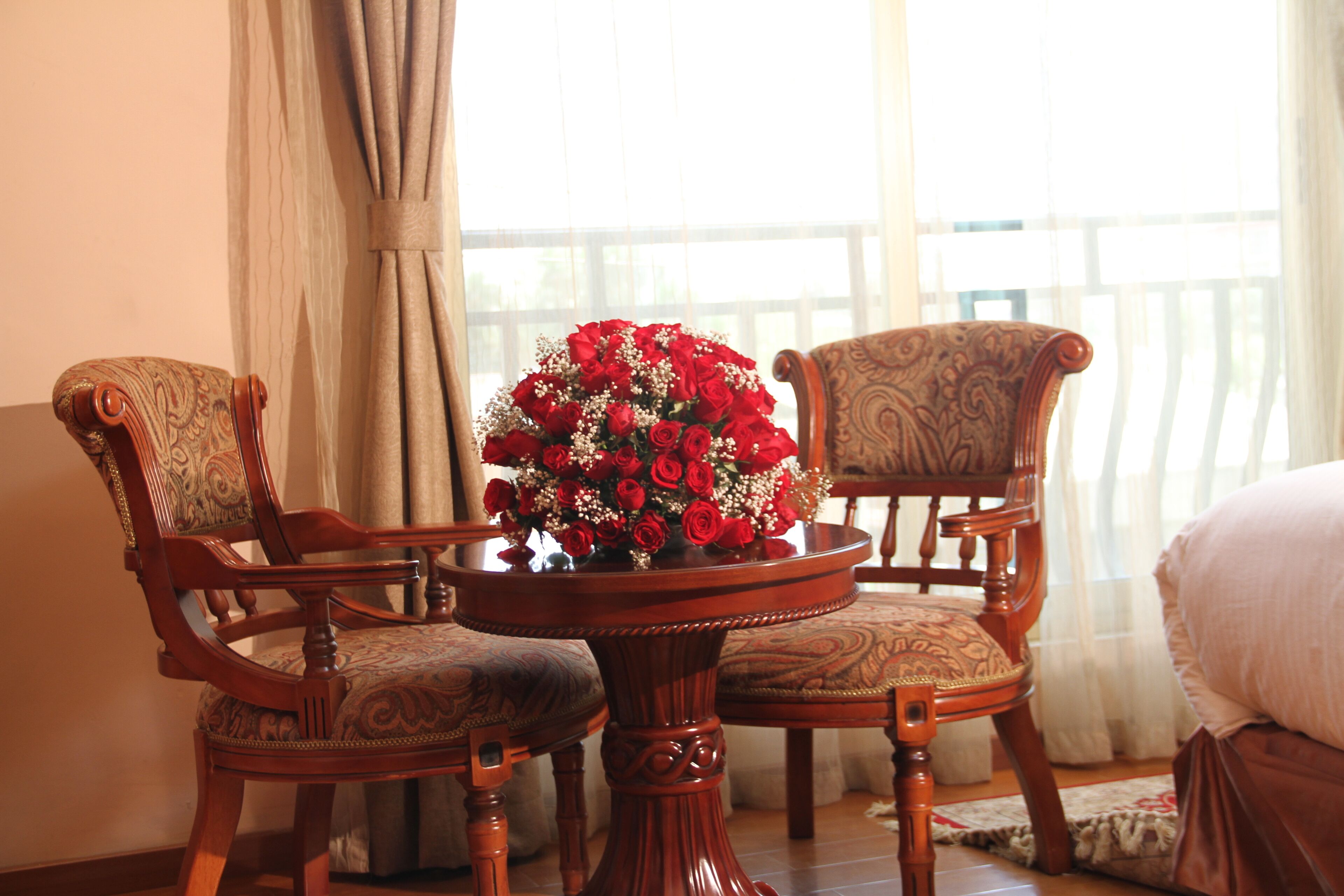 Une pièce comprenant deux fauteuils en bois richement décorés et une table agrémentée d’un arrangement floral.