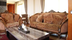 A living room with a sofa and armchairs, a coffee table, and a door leading to another room. - Emmad Apartment Hotel (Addis Ababa)