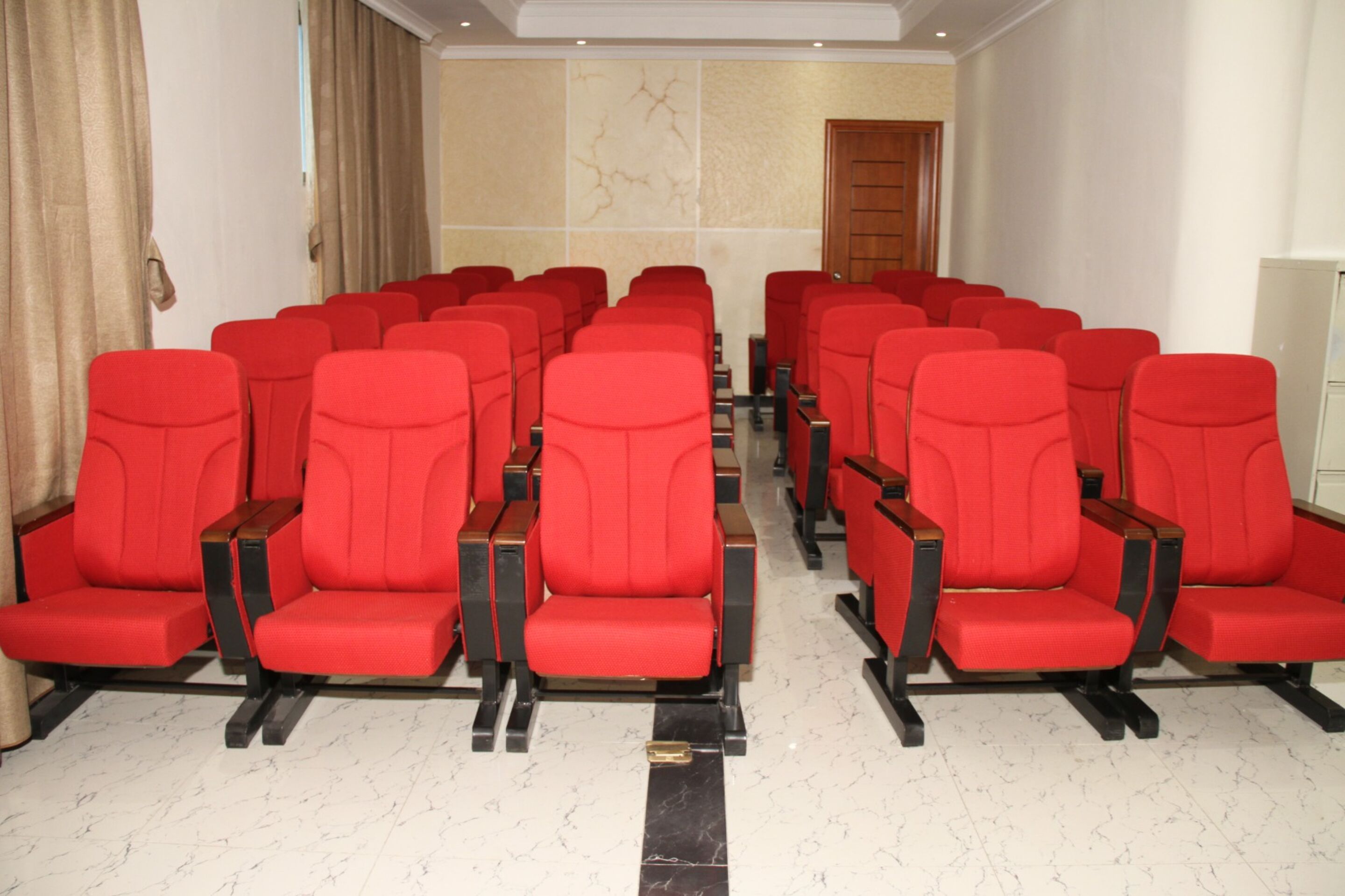 A row of red chairs with wooden armrests in a hotel lobby.