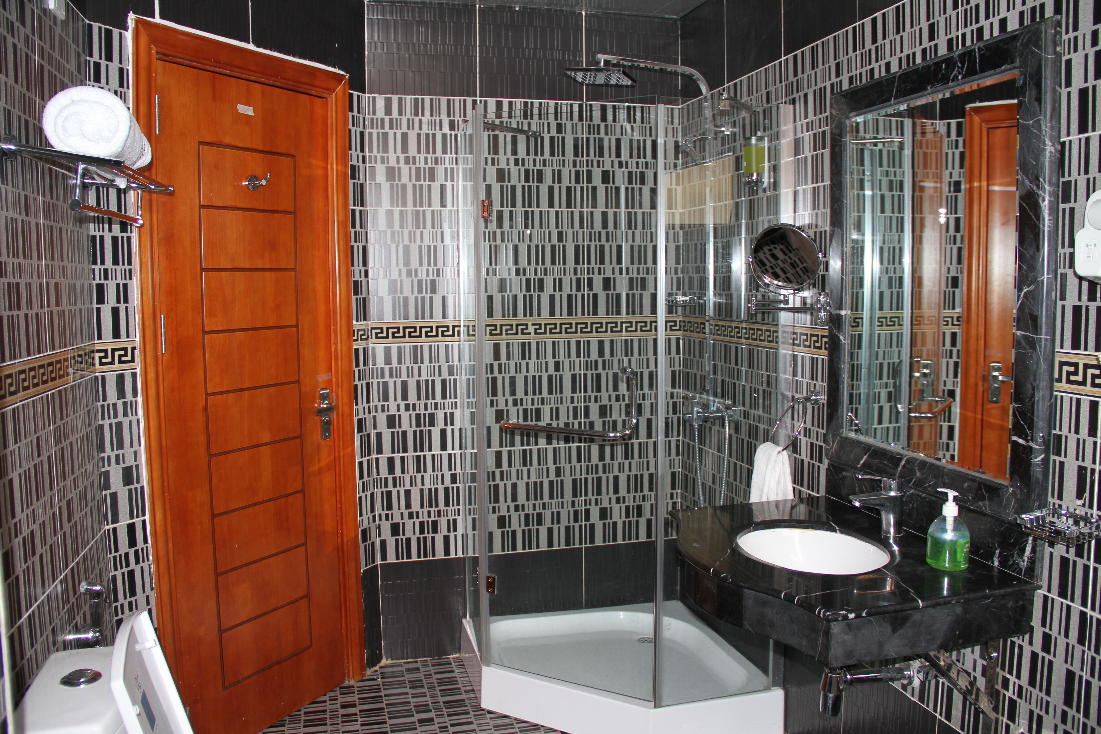 A bathroom with a wooden door, a glass-enclosed shower, a white sink, and a large mirror.