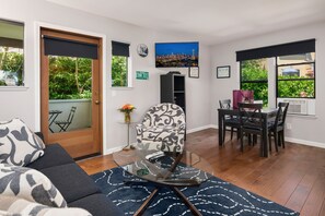 A modern living room with a sofa, a glass coffee table, a patterned armchair, and a dining area with a table and chairs. - Seattle Vacation Home: Thomas Lodge Vermont (Seattle)
