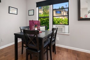 A dining area with a table, chairs, a window with a view of houses, and framed certificates on the wall. - Seattle Vacation Home: Thomas Lodge Vermont (Seattle)