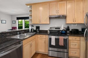 A modern kitchen with stainless steel appliances, wooden cabinets, granite countertops, and a window providing a view of greenery outside. - Seattle Vacation Home: Thomas Lodge Vermont (Seattle)