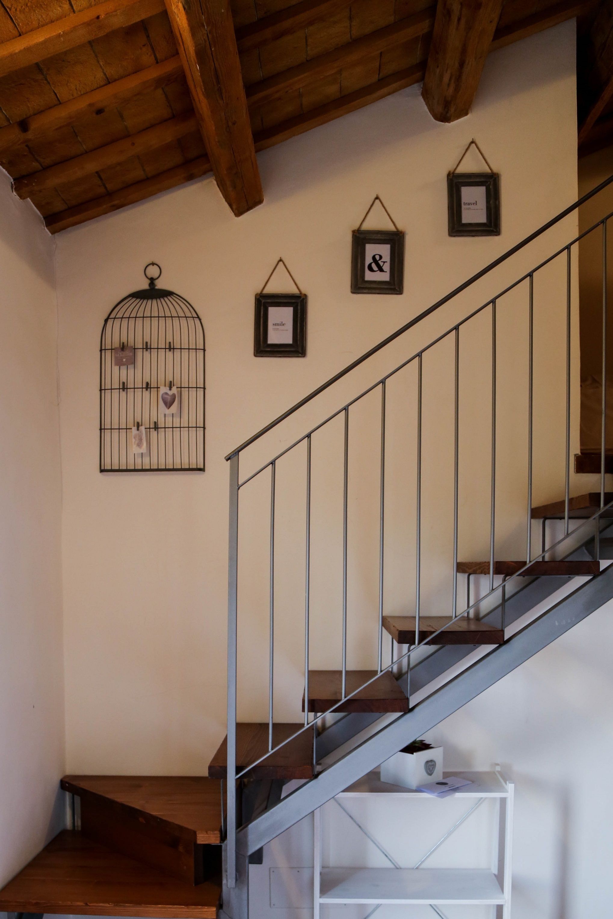Eine Treppe mit Holzdielen und einem Metallgeländer, die zu einer Zwischenebene mit einem weißen Regal und einem gerahmten Bild führt.
