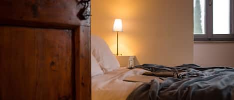 A bedroom with a wooden door, a bedside lamp, a bed with white bedding, and a window with a view of trees.