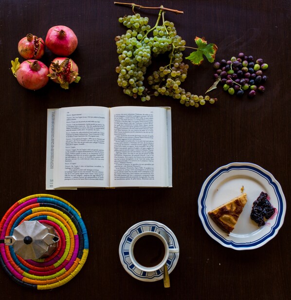 Um livro, um prato com comida, uma chávena e fios coloridos sobre uma mesa.