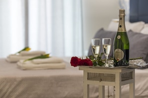 Une table soigneusement dressée, avec une bouteille de vin, deux verres et une rose rouge, posée sur une table de chevet recouverte d’une housse de couette blanche et agrémentée de coussins.