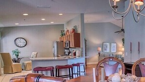 A dining area with wooden chairs, a chandelier, and a kitchen in the background. - Sabal Pointe at Majestic Palms 1004 Near beach Townhome. Sanibel/Captiva/Fort (Fort Myers)
