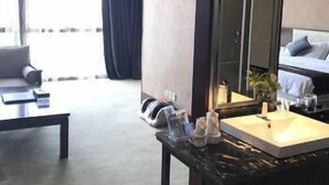 A hotel room with a large bed, a sitting area with a sofa and a coffee table, a bathroom with a mirror and toiletries, and a view of the outdoors. - Bo Jing International Hotel (Hangzhou)
