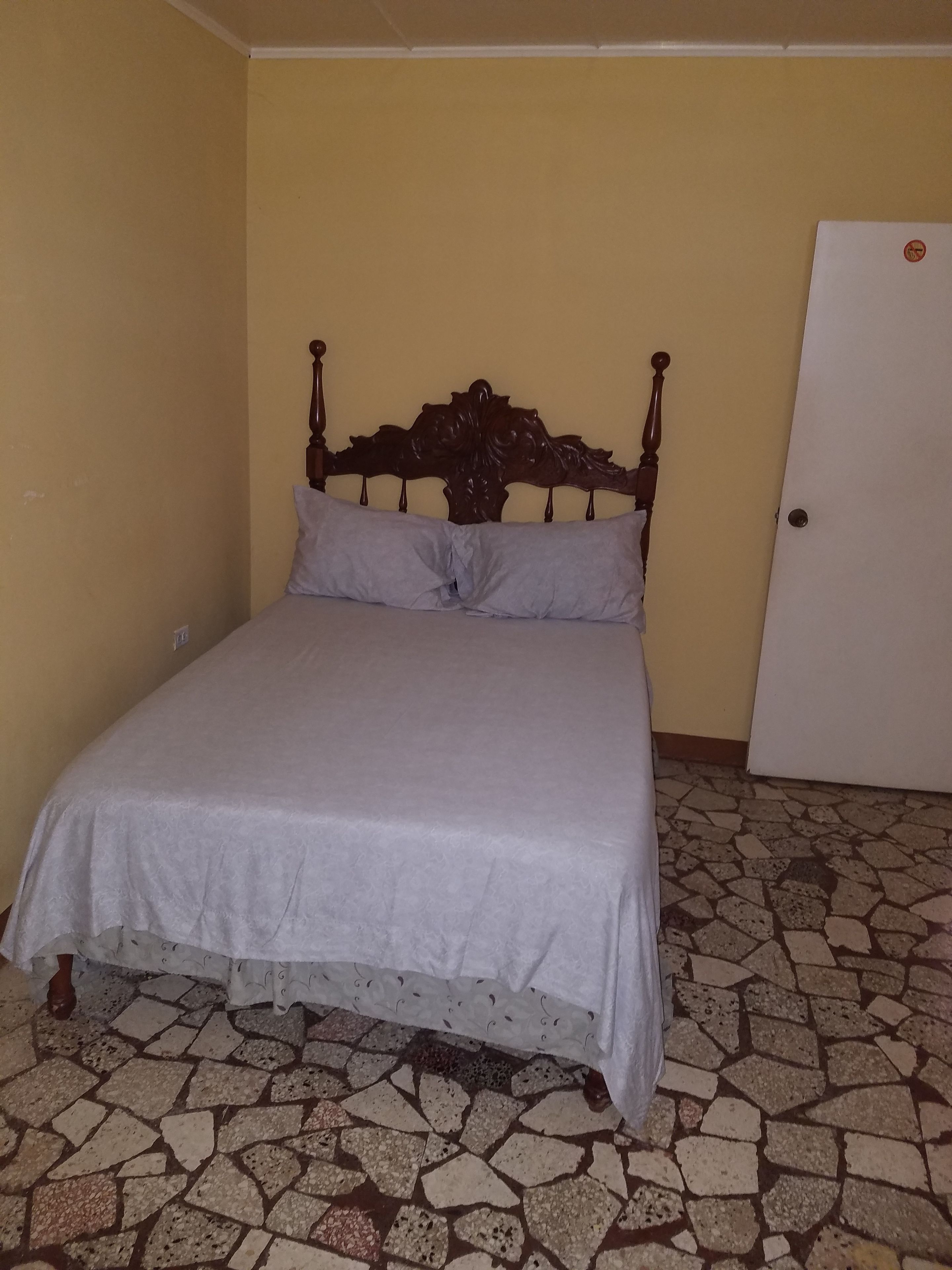 Un dormitorio con cama, una puerta y piso de baldosas.