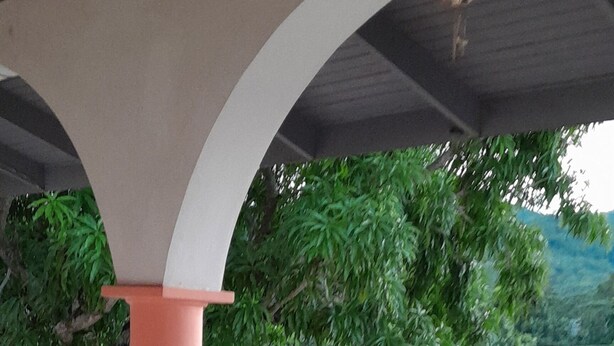 A covered outdoor area with a tiled floor, white railings, and a pink column. - The Cozy Family Inn Guesthouse (Port Antonio)