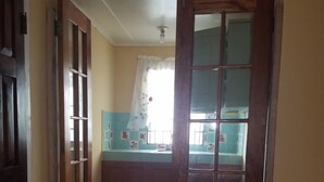 A narrow hallway with a tiled floor, a wooden door, and a window with a curtain. - The Cozy Family Inn Guesthouse (Port Antonio)