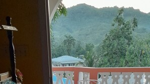 A room with a tiled floor, a table with chairs, and a view of a mountainous landscape. - The Cozy Family Inn Guesthouse (Port Antonio)