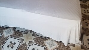A bed with a wooden headboard, white bedding, and a patterned floor. - The Cozy Family Inn Guesthouse (Port Antonio)
