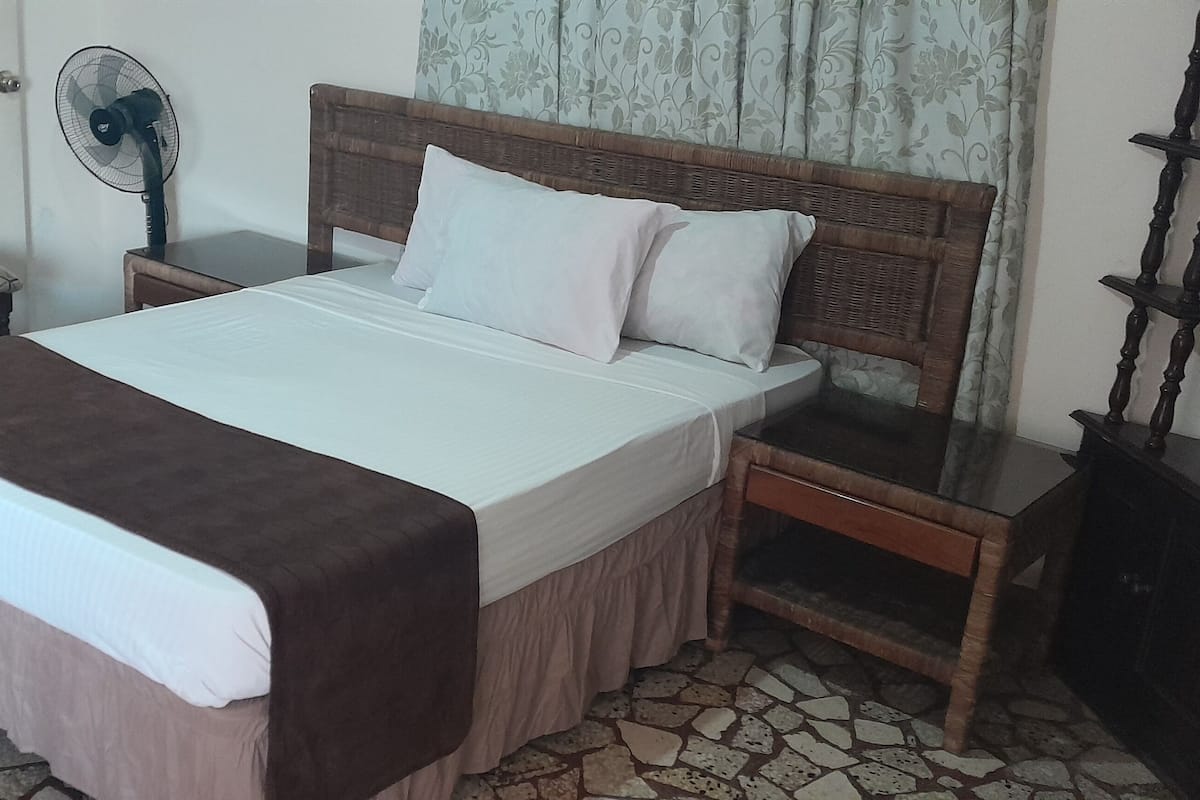 Een slaapkamer met een bed, nachtkastjes, een stoel, een ventilator en een kledingkast.