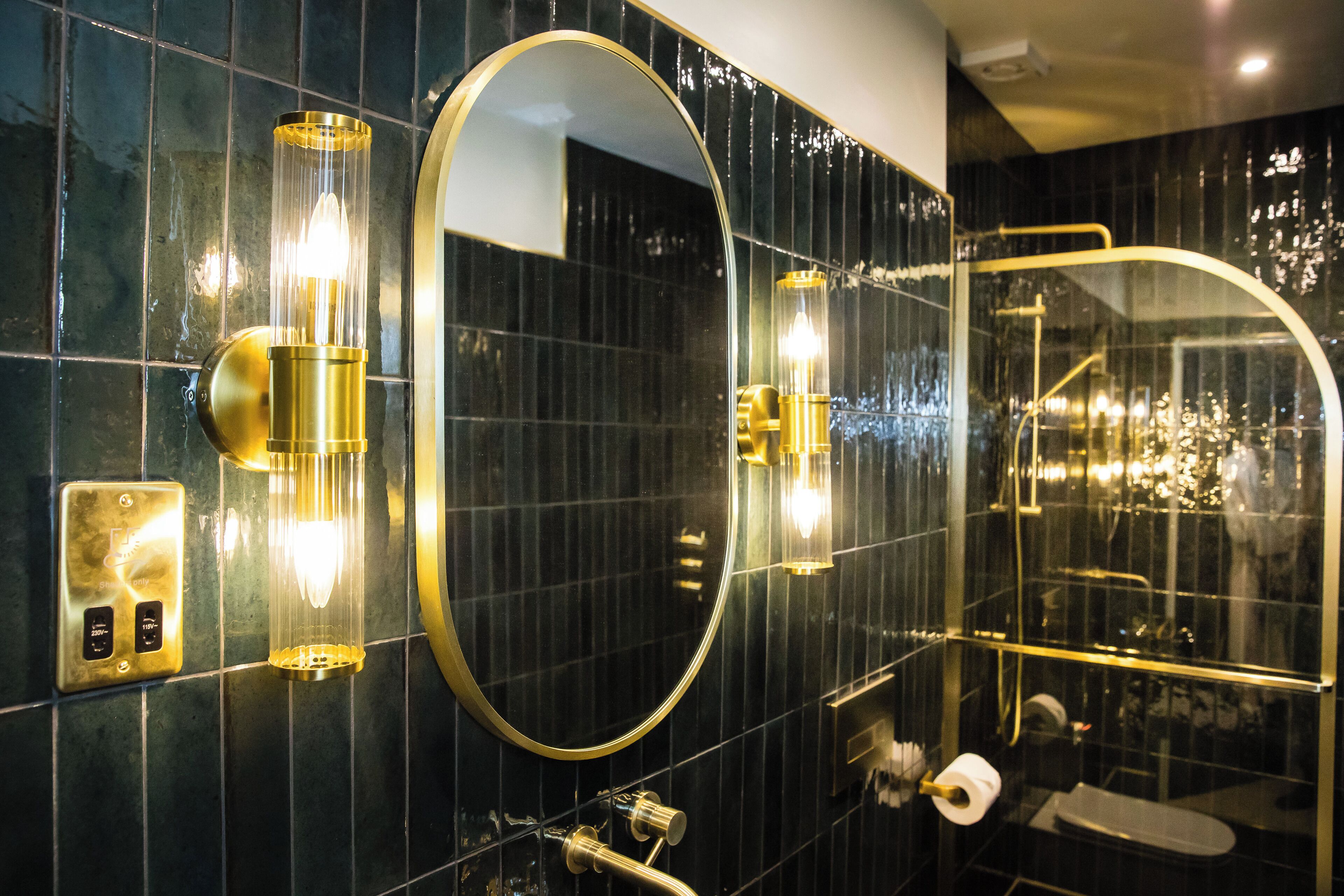 A modern bathroom with a large mirror, a wall-mounted light fixture, and a glass-enclosed shower area.