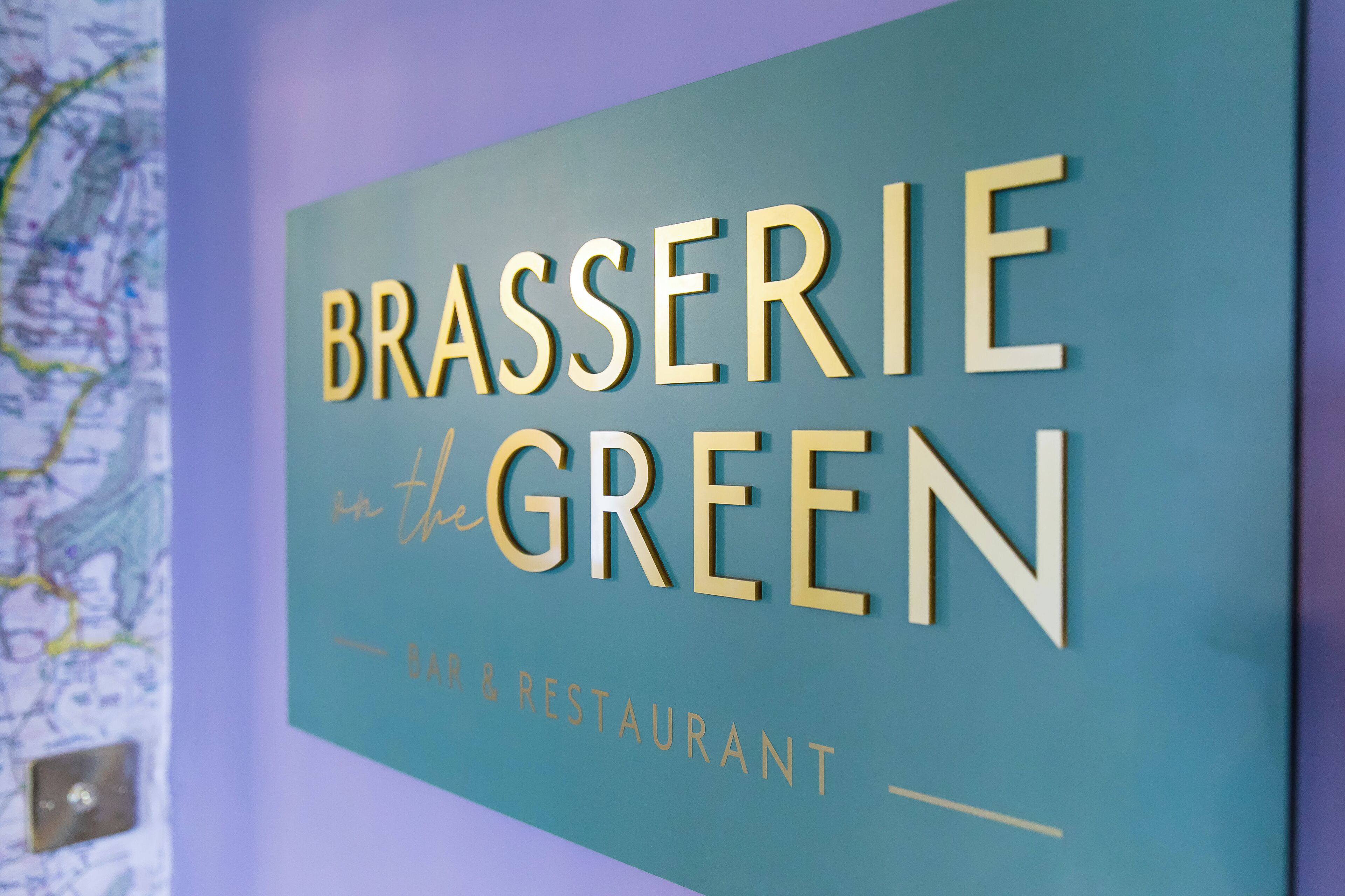 Skilt med teksten 'BRASSERIE in the GREEN' og 'BAR & RESTAURANT', der angiver en restaurant.