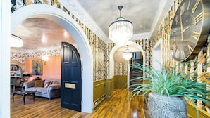 A hallway with wooden flooring, a large wall clock, and a potted plant.
