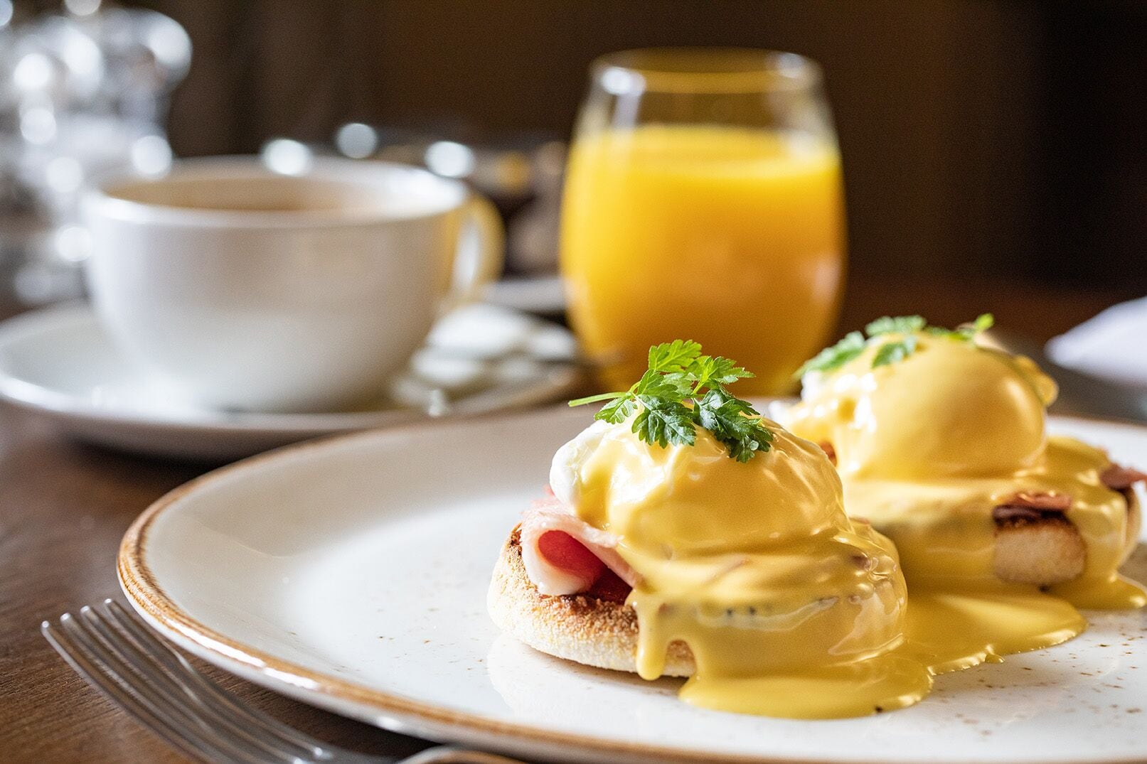 A breakfast setting with eggs benedict on a plate, a glass of orange juice, and a cup of coffee.