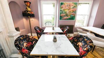 Un comedor con una mesa de mármol, sillas tapizadas con motivos florales, una lámpara de pie alta y un cuadro grande con flores en la pared.