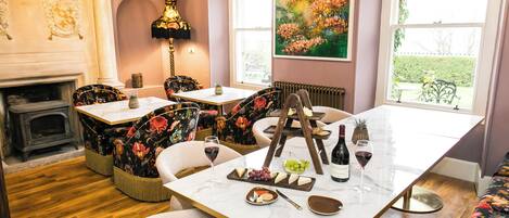 A dining area with a marble table, floral chairs, a fireplace, and a large window with a garden view.