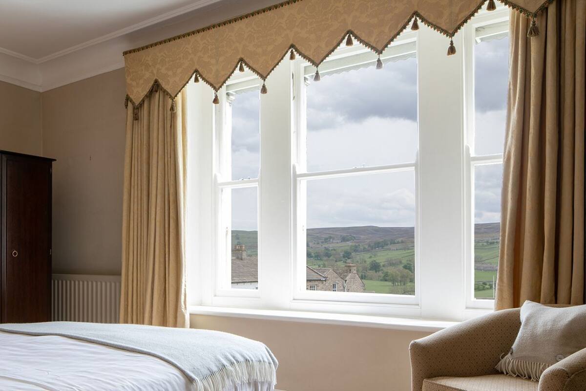 A bedroom with a bed, a chair, a wardrobe, and a window with a view of the countryside.