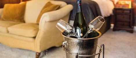 A room with a bed, a bedside table, a nightstand, a lamp, and a bottle of champagne in a metal bucket.