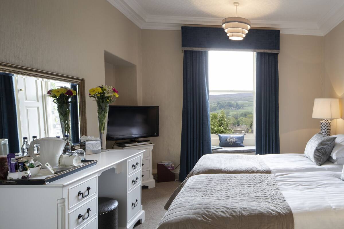 A hotel room with a large bed, a TV, a desk with a computer, and a window with curtains.