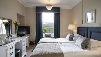 Habitación de hotel con una cama grande, televisión, escritorio con ordenador y ventana con cortinas.