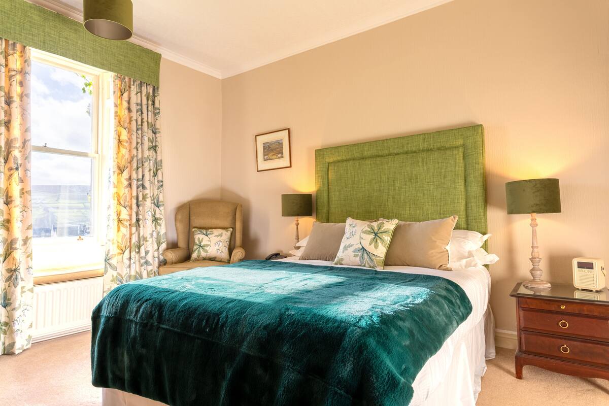 A neatly arranged bedroom with a bed, two bedside tables, a chair, and a window with curtains.