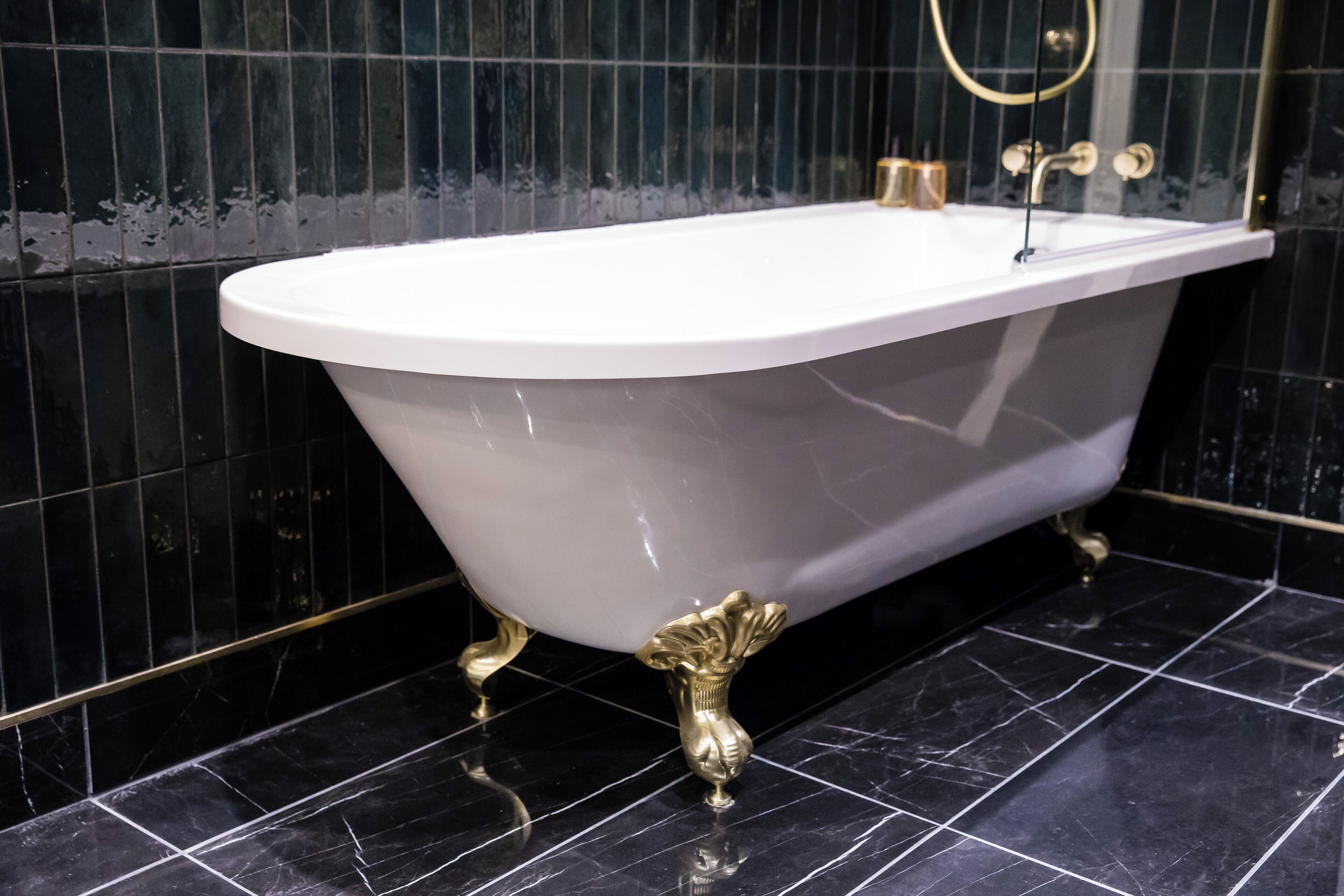 Eine freistehende Badewanne mit goldenen Füßen in einem Badezimmer mit schwarzen Fliesenwänden und -boden.