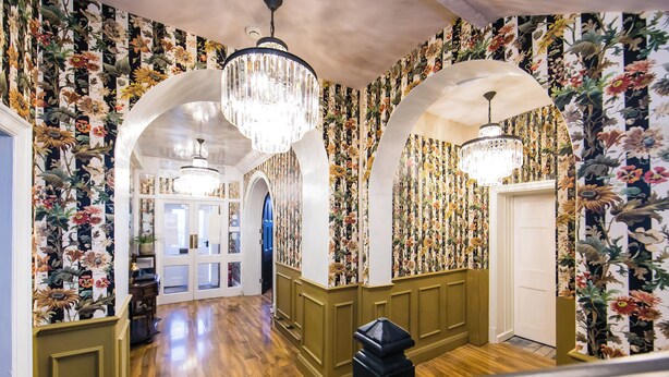 A hallway with floral wallpaper, wooden flooring, and chandeliers.
