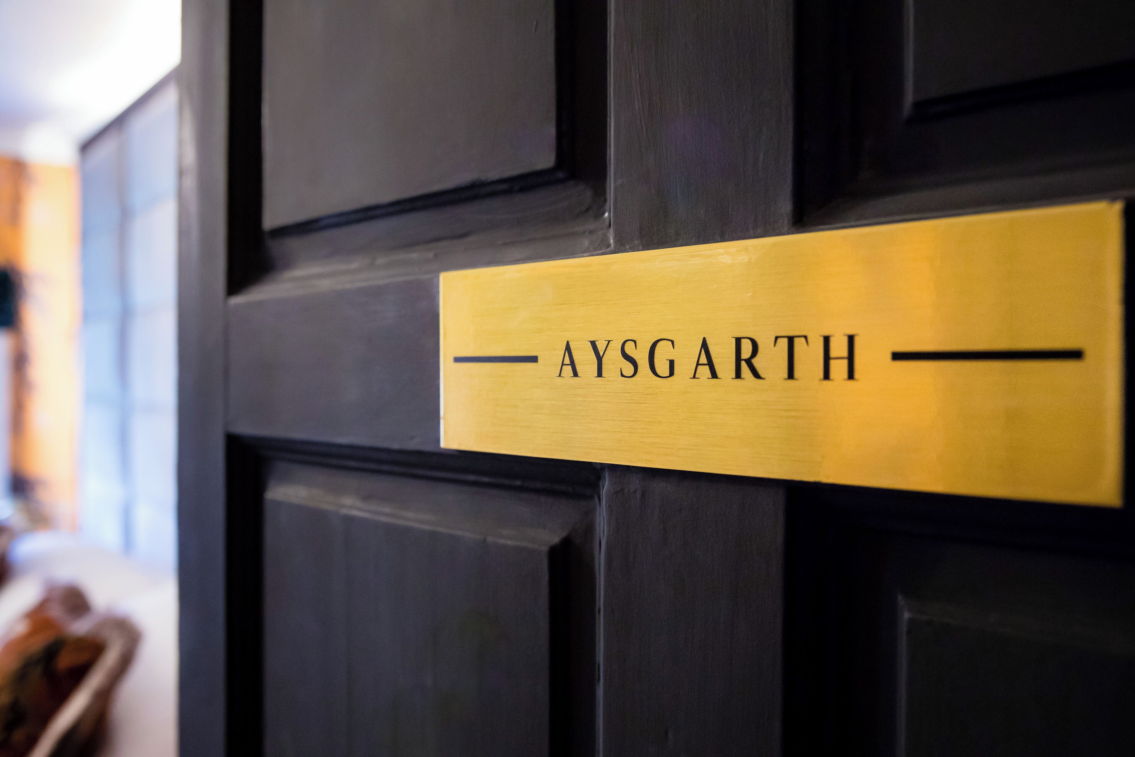 Une porte noire avec une plaque dorée portant le nom « AYSGARTH ».