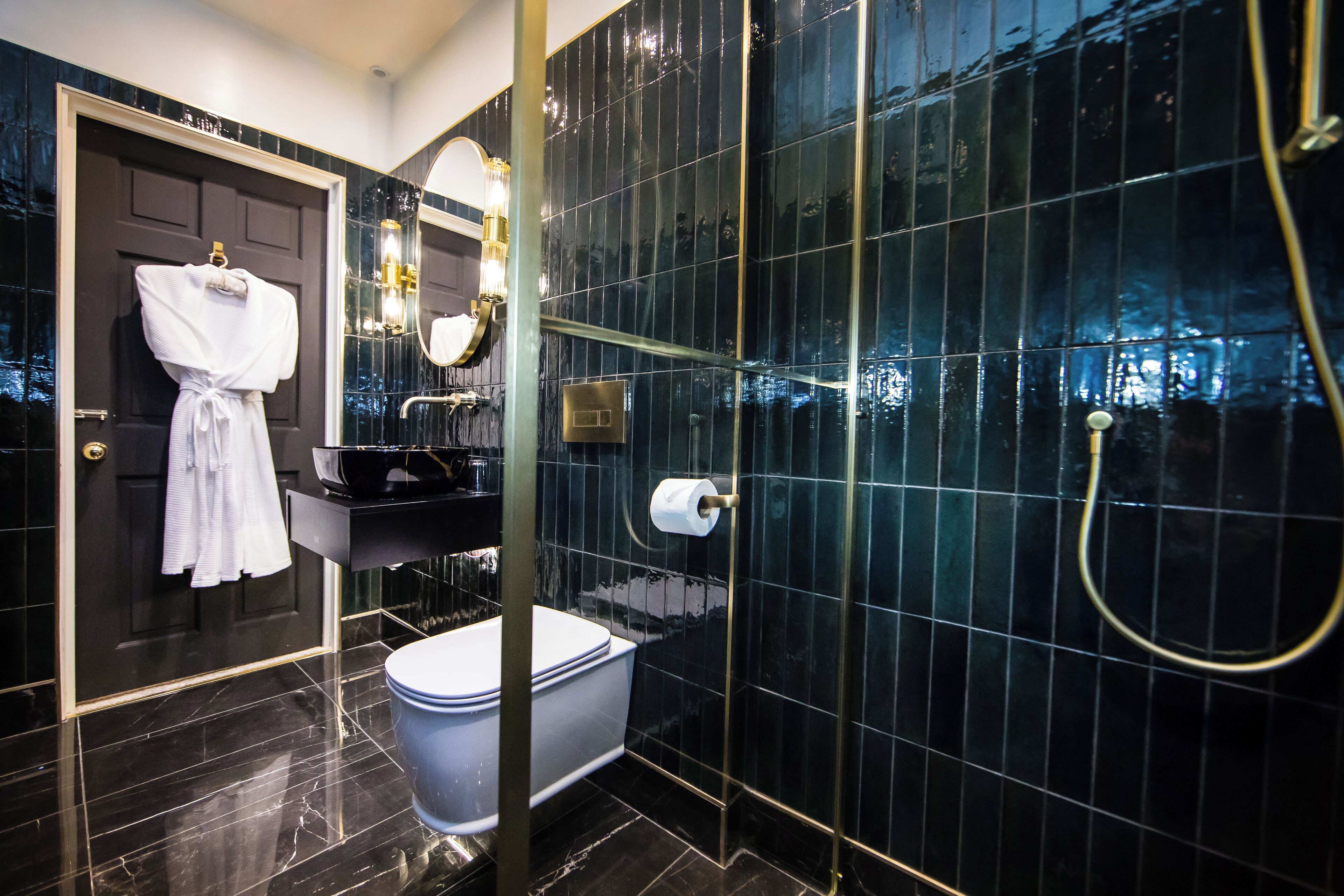 A modern bathroom with a black tiled wall, a white bathtub, a white toilet, and a glass-enclosed shower area.