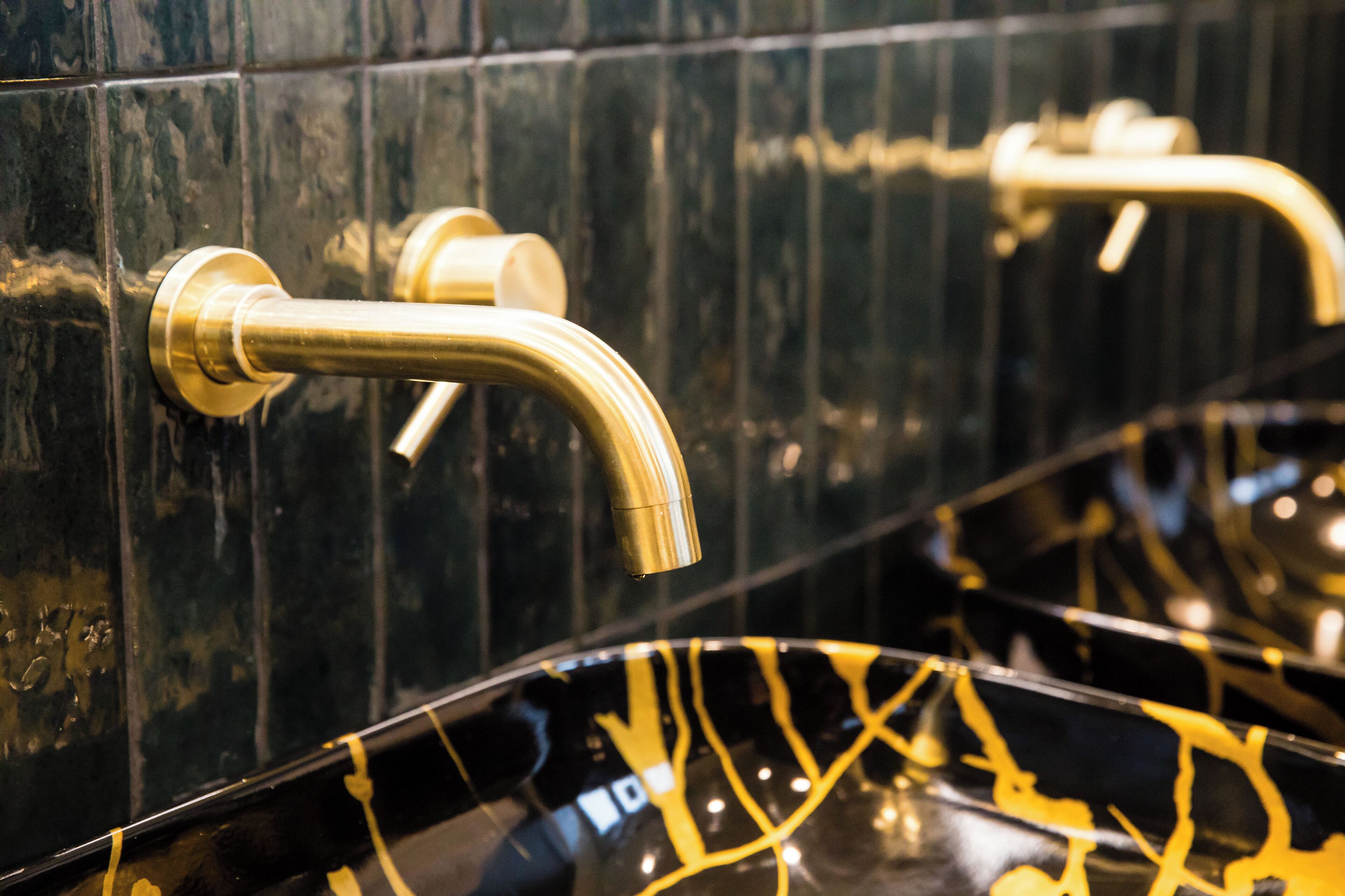 A bathroom with black marble walls and gold fixtures, including a curved faucet and a sink with a reflective surface.