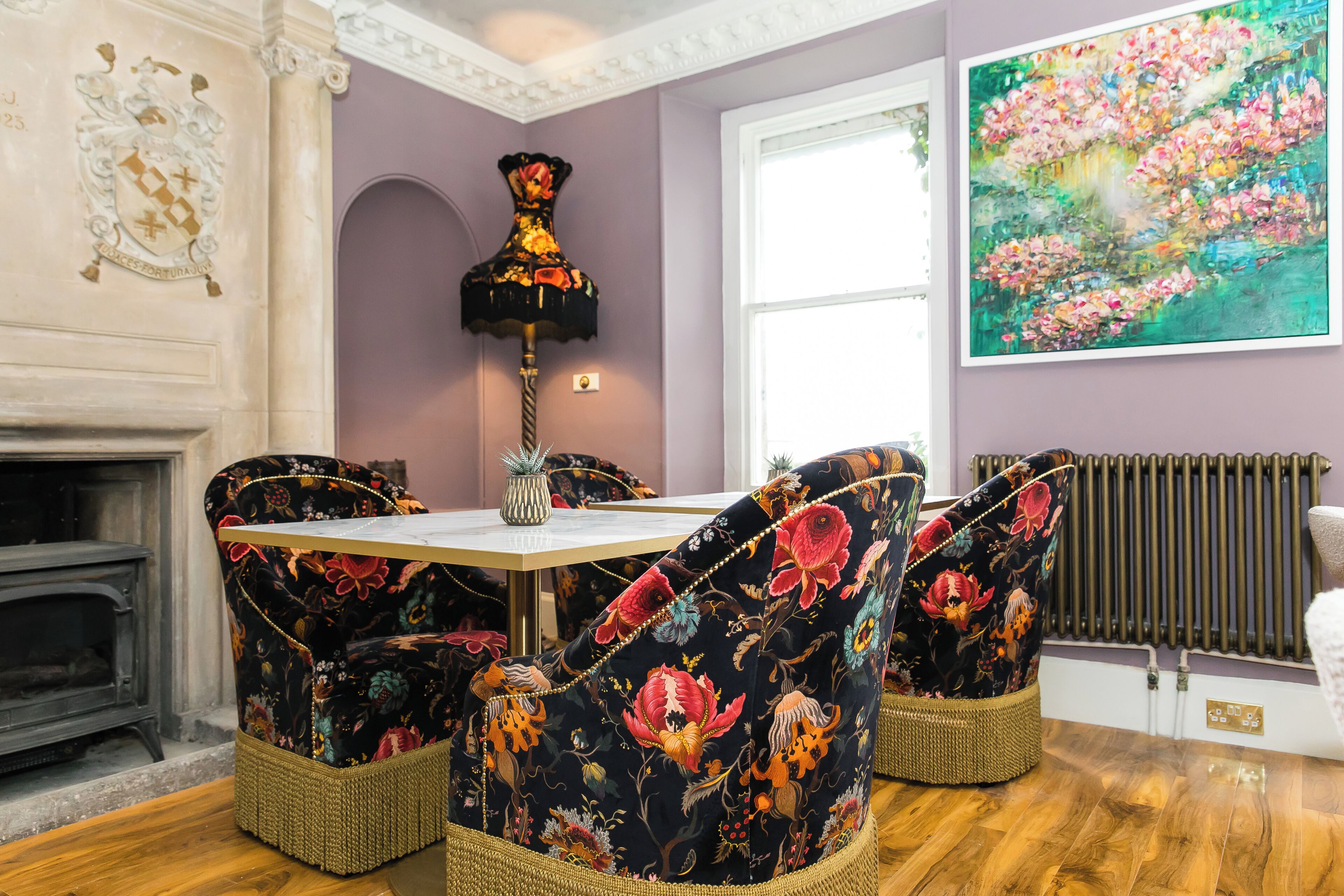 A dining area with a table and chairs, a fireplace, a radiator, and a floral painting on the wall.